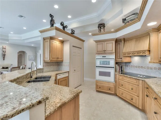 Kitchen with light stone counters, white appliances, a tray ceiling, premium range hood, and sink