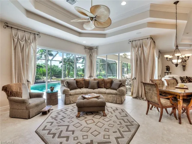Living room with ceiling fan, a raised ceiling, light tile patterned flooring, and crown molding