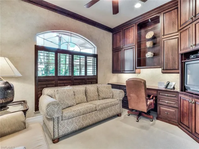 Office space with ornamental molding, built in desk, ceiling fan, and light carpet