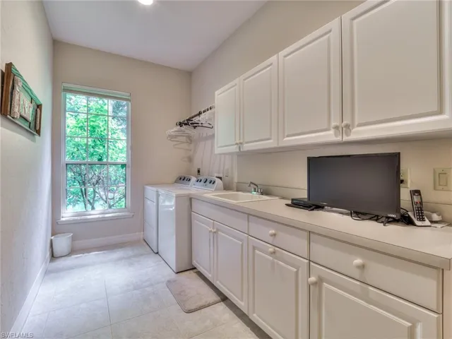 Clothes washing area featuring cabinets, light tile patterned flooring, washer and dryer, and sink