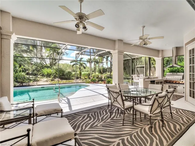 View of swimming pool with glass enclosure, area for grilling, ceiling fan, and a patio