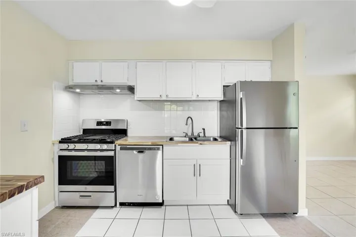 Kitchen with appliances with stainless steel finishes, under cabinet range hood, decorative backsplash, and white cabinets