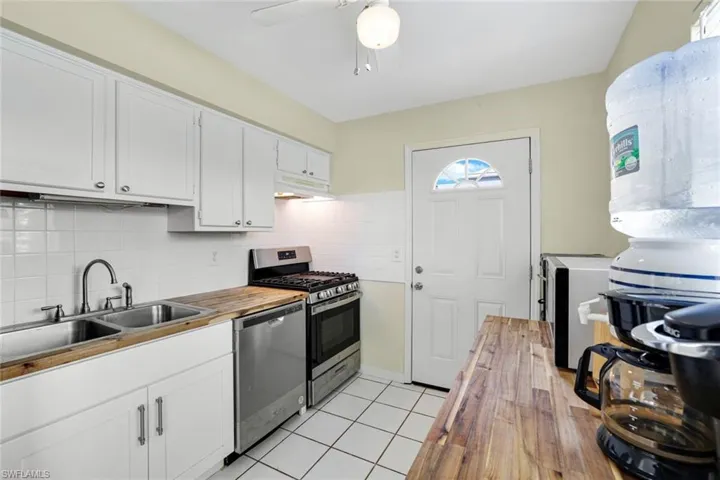 Kitchen featuring stainless steel appliances, butcher block countertops, under cabinet range hood, and white cabinets