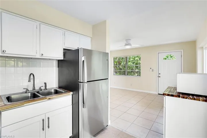 Kitchen featuring freestanding refrigerator, decorative backsplash, light tile patterned floors, ceiling fan, and white cabinetry