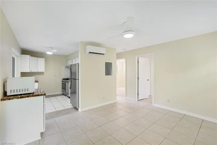 Kitchen with stainless steel appliances, a wall unit AC, light tile patterned floors, ceiling fan, and white cabinets