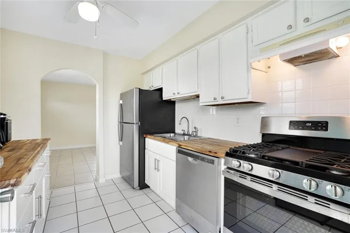 Kitchen with butcher block counters, stainless steel appliances, under cabinet range hood, arched walkways, and a ceiling fan