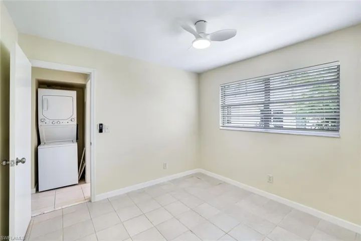 Empty room with stacked washer and clothes dryer, a ceiling fan, and light tile patterned flooring