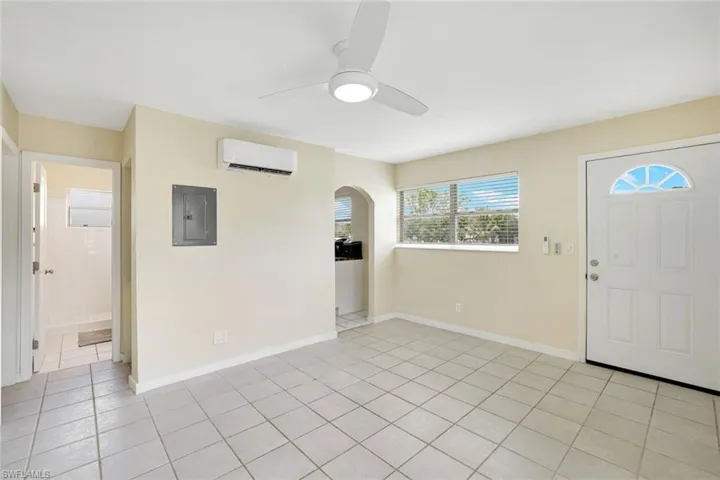 Foyer entrance with a wall unit AC, electric panel, ceiling fan, light tile patterned floors, and arched walkways
