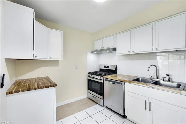 Kitchen with stainless steel appliances, under cabinet range hood, backsplash, white cabinetry, and light tile patterned floors