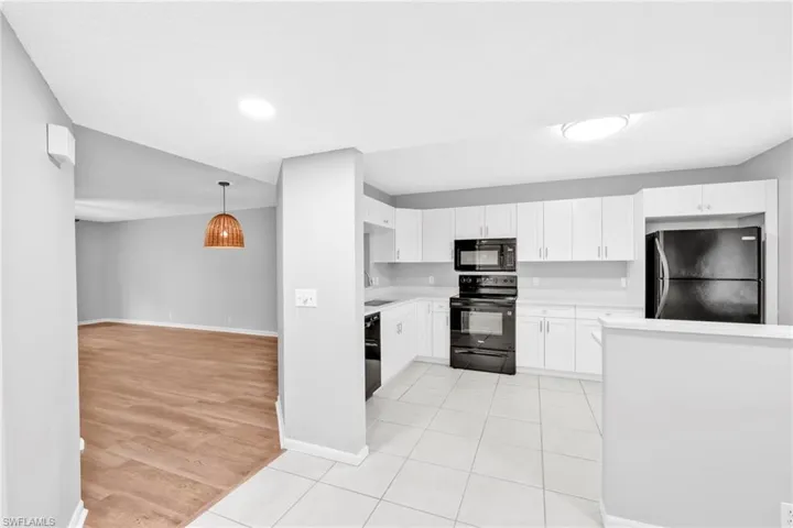 Kitchen with black appliances, light tile patterned floors, white cabinetry, pendant lighting, and open floor plan
