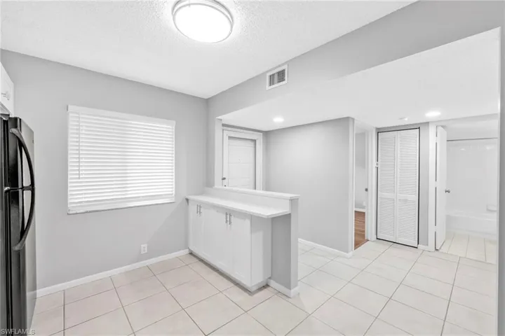 Kitchen with a peninsula, white cabinets, freestanding refrigerator, light countertops, and a textured ceiling