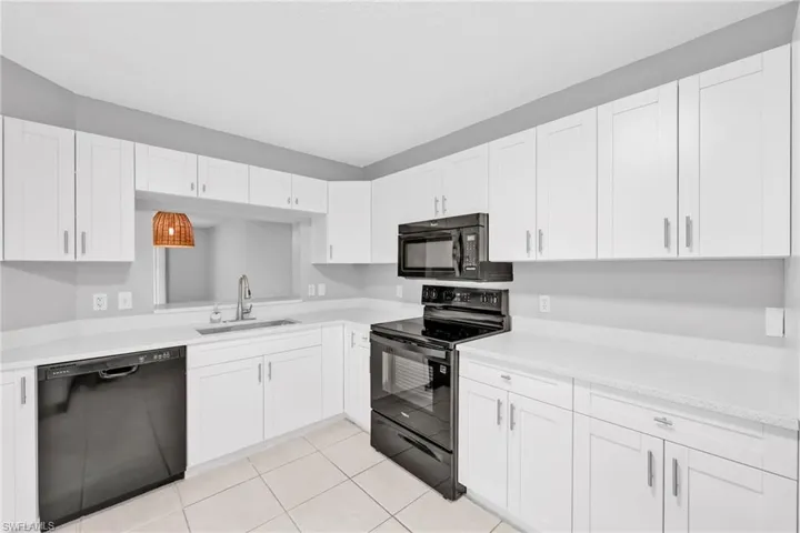 Kitchen with black appliances, white cabinets, and light stone counters