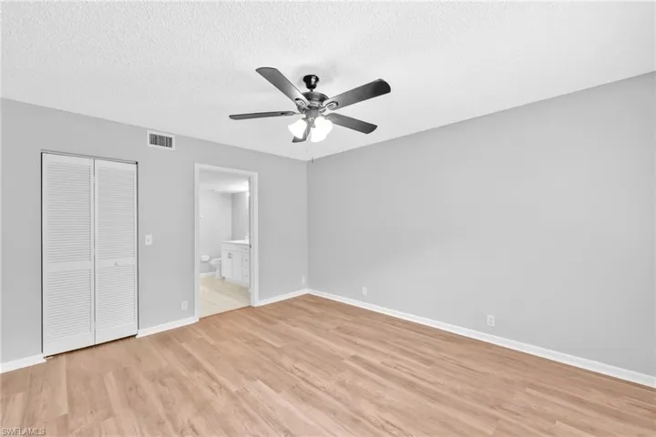 Unfurnished bedroom with a textured ceiling, a closet, light wood-style flooring, ceiling fan, and ensuite bathroom