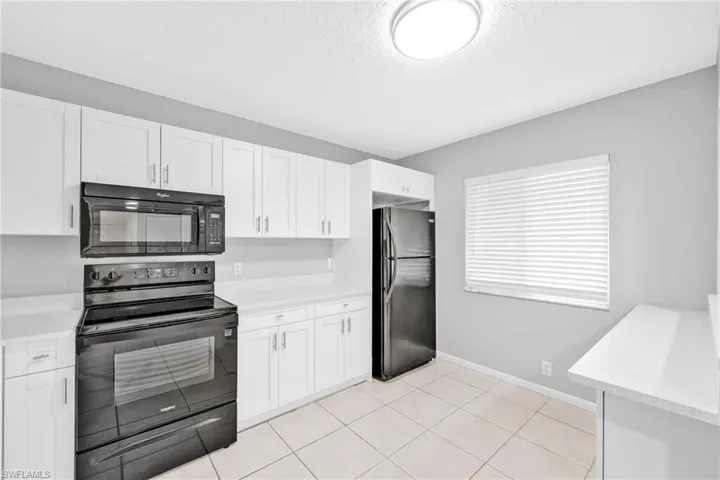 Kitchen featuring black appliances, white cabinets, a textured ceiling, light tile patterned flooring, and light stone countertops