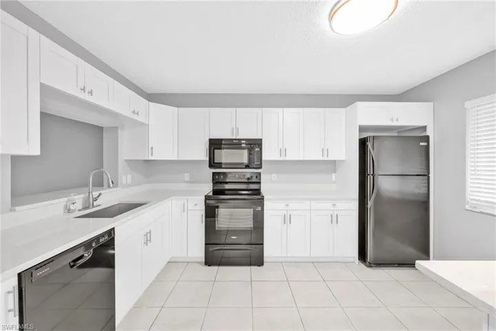 Kitchen with black appliances, white cabinetry, light stone counters, light tile patterned floors, and a textured ceiling