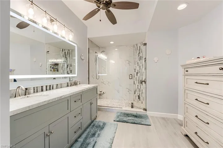 Full bathroom with double vanity, a marble finish shower, a ceiling fan, light wood-style flooring, and recessed lighting