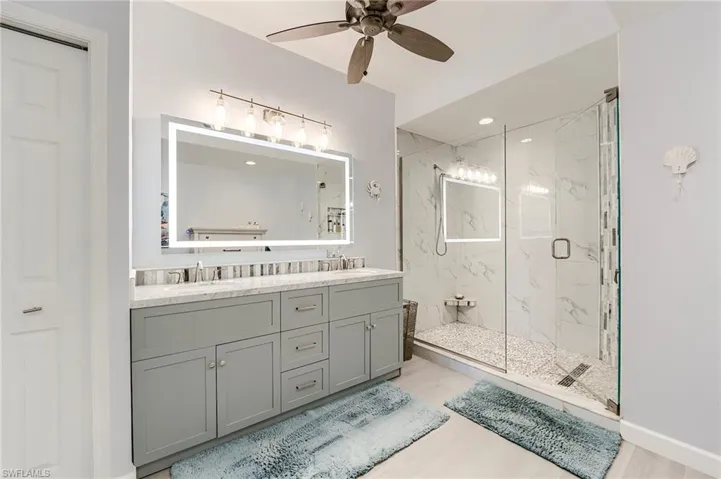 Full bath with double vanity, a marble finish shower, ceiling fan, recessed lighting, and light wood-type flooring