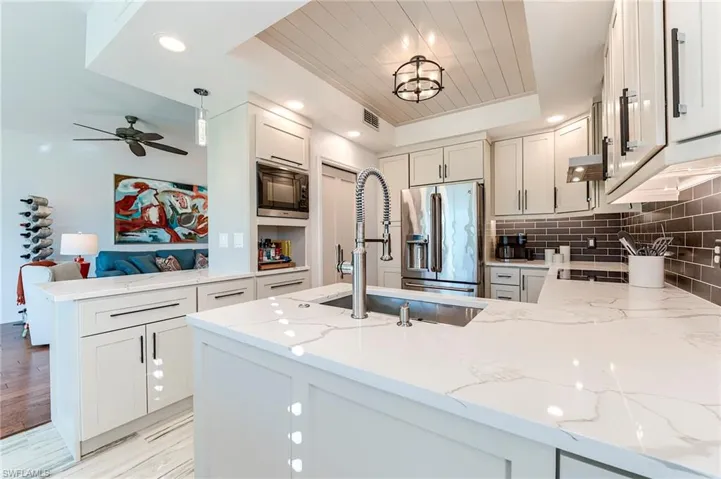 Kitchen featuring a peninsula, light stone counters, a raised ceiling, recessed lighting, and stainless steel fridge