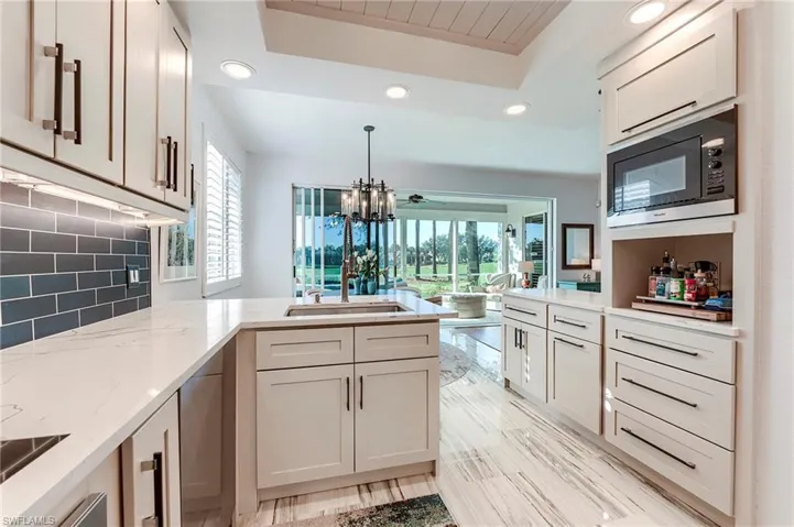 Kitchen with recessed lighting, a peninsula, built in microwave, decorative backsplash, and light stone counters