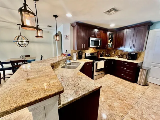 Kitchen with pendant lighting, backsplash, stainless steel appliances, sink, and light stone countertops