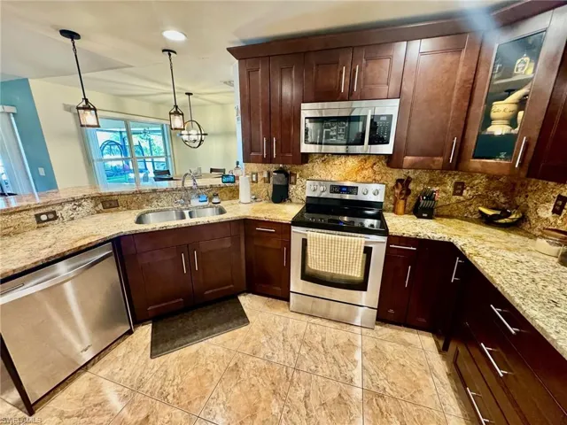 Kitchen with light stone countertops, stainless steel appliances, sink, and decorative backsplash
