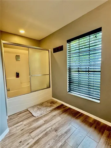 Bathroom with wood-type flooring and combined bath / shower with glass door