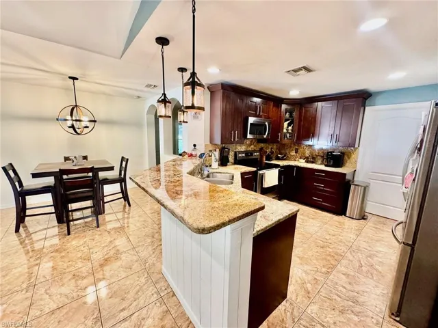 Kitchen with stainless steel appliances, kitchen peninsula, sink, light stone countertops, and hanging light fixtures