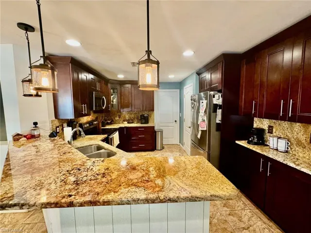 Kitchen with hanging light fixtures, kitchen peninsula, light stone countertops, and appliances with stainless steel finishes