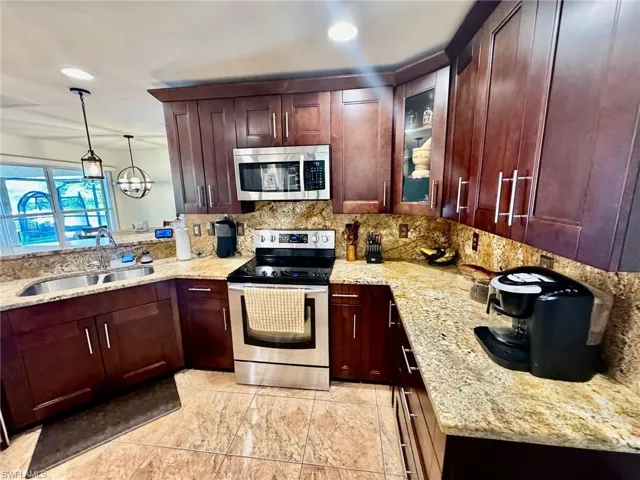Kitchen featuring tasteful backsplash, stainless steel appliances, sink, light stone countertops, and hanging light fixtures