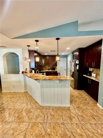 Kitchen featuring stainless steel refrigerator, kitchen peninsula, light stone counters, decorative backsplash, and vaulted ceiling
