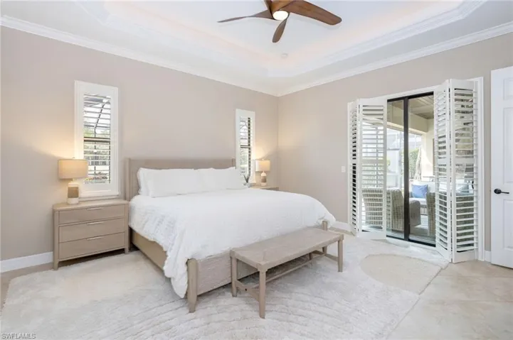 Tray ceiling with crown molding, ceiling fan, plantation shutters, and sliding glass doors with louvered bi-fold panels