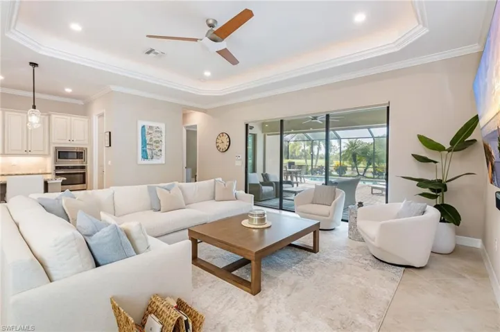 Tray ceiling with crown molding, recessed lighting, ceiling fan, and sliding glass doors leading to an outdoor screened enclosure