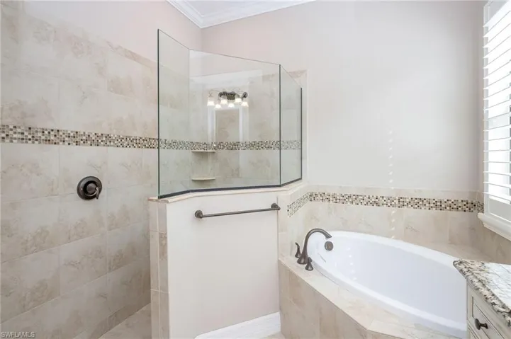 Walk-in shower with clear glass enclosure, a built-in tub, and tiled walls with a decorative mosaic accent