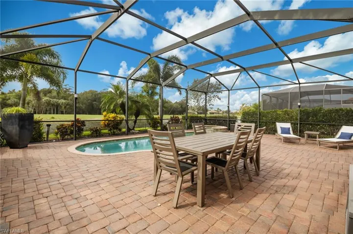 Screened enclosure featuring a swimming pool, expansive paver patio, and lush landscaping