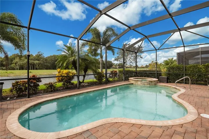 Screened lanai featuring a freeform swimming pool, integrated spa, and brick-style paver decking
