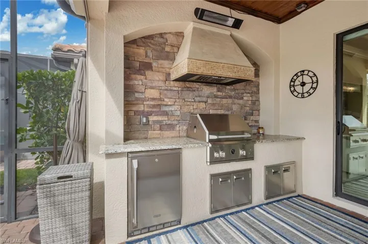 Built-in outdoor kitchen featuring stainless steel grill, integrated refrigerator, stone accent wall, and granite countertops