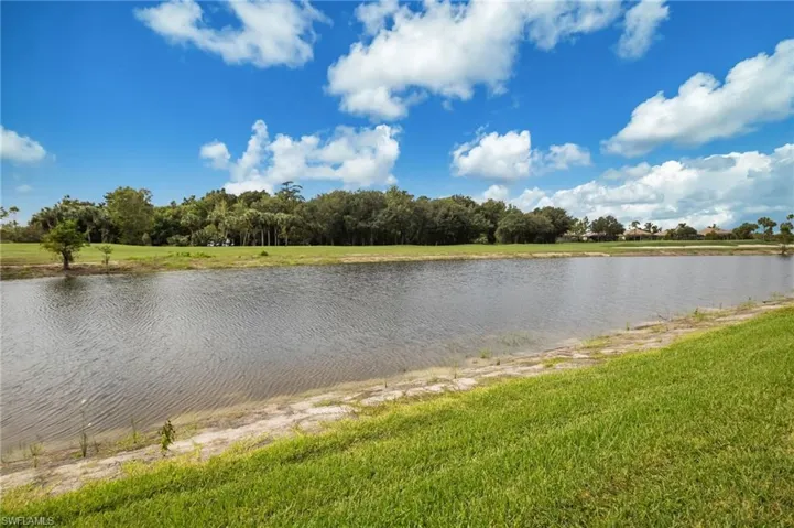 Expansive waterfront setting featuring a tranquil pond, lush green lawn, and mature trees