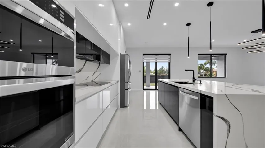 Kitchen with modern cabinets, stainless steel appliances, white cabinets, light stone counters, and recessed lighting