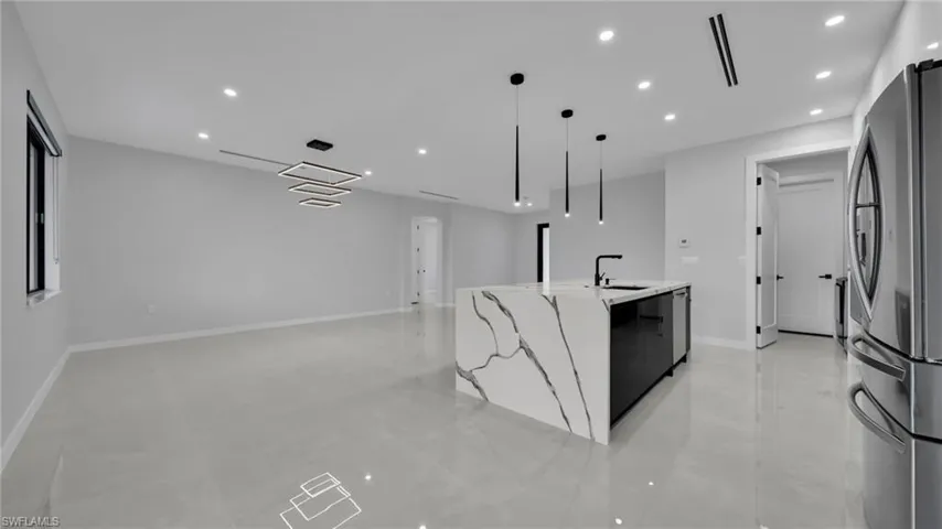 Kitchen with recessed lighting, appliances with stainless steel finishes, light stone countertops, hanging light fixtures, and a center island with sink