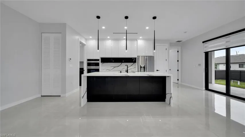 Kitchen with modern cabinets, white cabinetry, a large island with sink, hanging light fixtures, and appliances with stainless steel finishes