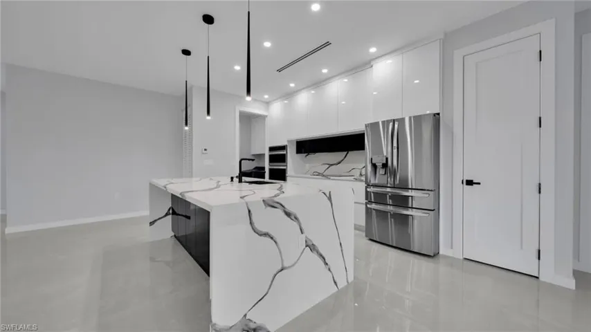 Kitchen with stainless steel appliances, decorative light fixtures, modern cabinets, recessed lighting, and a center island with sink