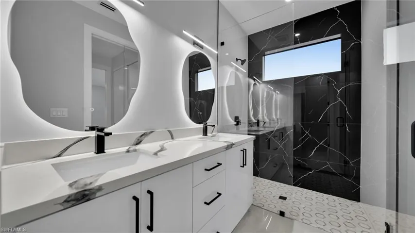 Bathroom with double vanity and a marble finish shower