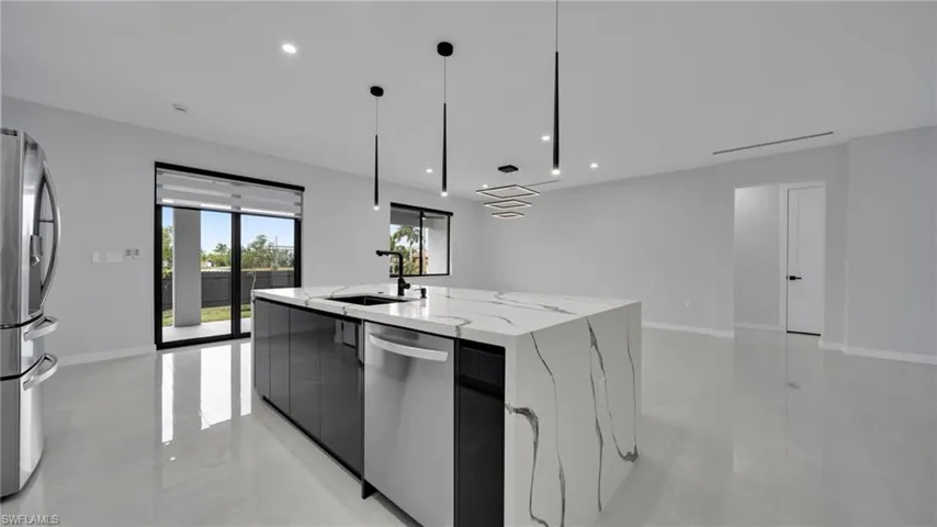 Kitchen with modern cabinets, light stone counters, stainless steel appliances, pendant lighting, and an island with sink
