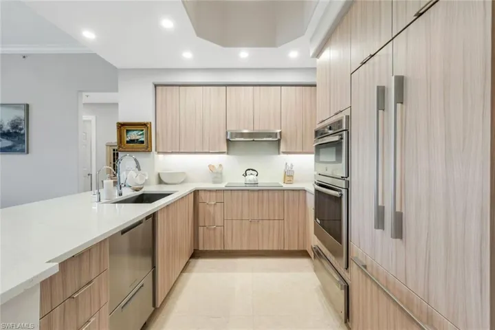 Kitchen with a sink, modern cabinets, range hood, appliances with stainless steel finishes, and light brown cabinetry