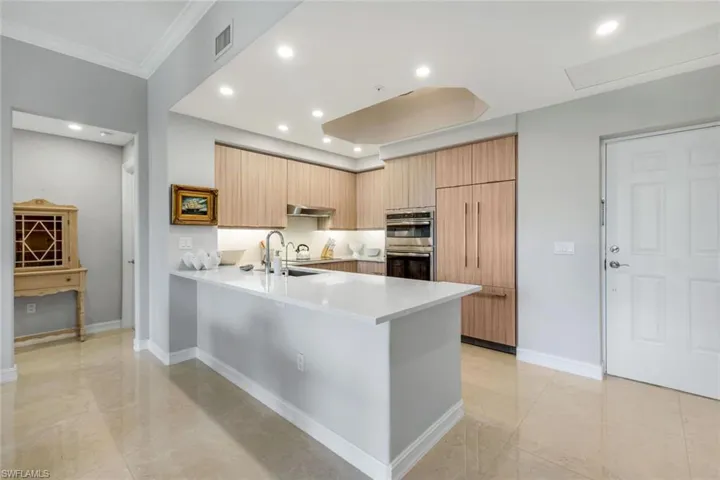 Kitchen with stainless steel double oven, light countertops, a peninsula, ventilation hood, and ornamental molding