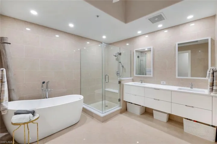 Full bathroom with tile walls, a stall shower, a freestanding bath, double vanity, and recessed lighting