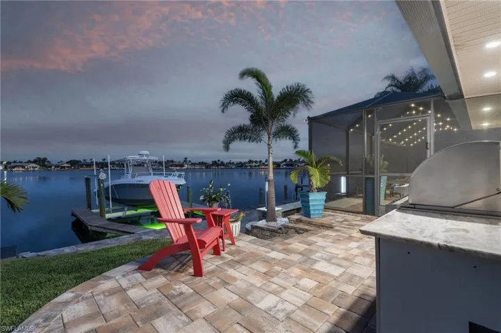 Patio terrace at dusk with a lanai, grilling area, a water view, and a boat dock