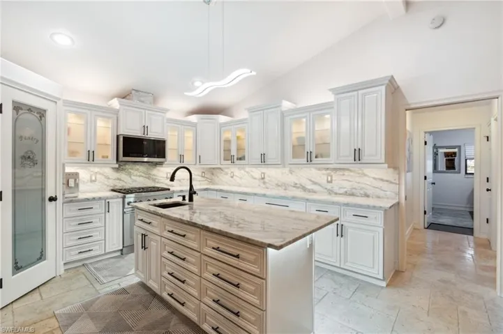 Kitchen with white cabinets, lofted ceiling with beams, sink, an island with sink, and appliances with stainless steel finishes