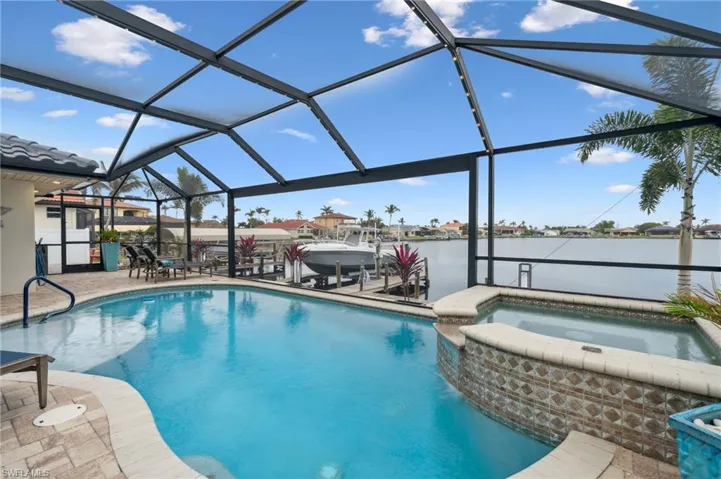 View of pool with glass enclosure, a water view, an in ground hot tub, and a patio