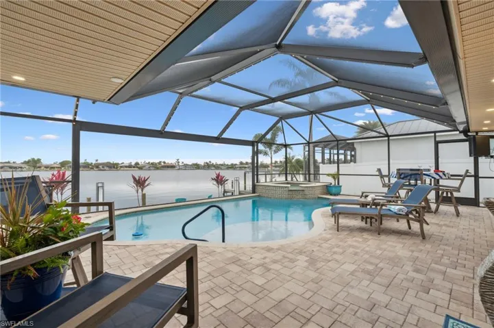View of swimming pool featuring an in ground hot tub, a water view, glass enclosure, and a patio area